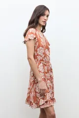 Vestido corto cruzado de color terracota con estampado floral blanco, escote en V, mangas cortas con vuelo y volados en el borde de la falda y la abertura.