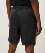 Bermuda deportiva de tejido plano de poliamida, color negro y gris claro, con bloques de color reflectivo en la parte inferior. Presenta cintura elástica con amarre y un pequeño logo de la NASA en la pierna derecha.