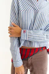 Camisa de corte oversize y estilo casual, confeccionada en algodón negro con costuras a contratono en color blanco. Presenta cuello camisero, cierre frontal parcial, mangas largas y un bordado distintivo en el puño.