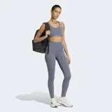 Top deportivo Adidas de soporte medio, color gris, con diseño racer-back y logo de la marca estampado en el frente. Confeccionado en tejido técnico transpirable con tecnología Climacool y almohadillas removibles.