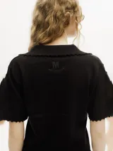 Chomba de punto negro, de manga corta, con cuello tipo polo, escote en V abotonado con detalles de crochet en los bordes y terminaciones acanaladas.