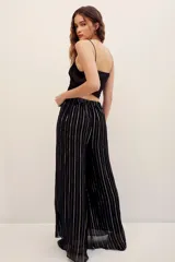 Pantalón fluido de tiro medio con diseño de rayas verticales metalizadas en tono dorado sobre base negra, corte amplio y silueta recta.