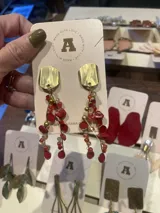 Aros colgantes con base metálica dorada de forma irregular y estructura de múltiples hilos con cuentas de piedra roja, cristal y detalles metálicos.