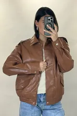 Chaqueta de ecocuero color marrón, de corte oversize, con cuello clásico, cierre frontal metálico, bolsillos laterales con solapa y puños con broches a presión.