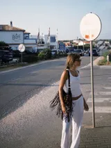 Bolso de hombro estilo boho confeccionado en gamuza color bordó. Presenta un diseño semicircular decorado con tachas metálicas plateadas dispuestas en líneas curvas y flecos largos en todo el borde inferior. Cuenta con cierre superior y correa ajustable para llevar al hombro.