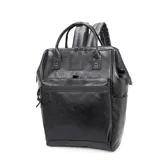 Mochila negra de cuero sintético con diseño estructurado y múltiples cierres. Presenta dos asas superiores, correas ajustables para llevar como mochila, bolsillo frontal con cierre horizontal y bolsillos laterales abiertos. Tiene un parche con el logo "TROY" en la parte superior central.