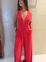 Mono largo de color fucsia, sin mangas, con escote en V profundo y detalle de tul transparente en el centro del pecho. Presenta bolsillos laterales y pantalón de corte amplio y fluido.