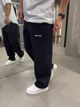 Pantalón deportivo negro de algodón con corte oversize, cintura elástica, bolsillos laterales, costuras frontales en relieve y pequeño estampado en la pierna izquierda.