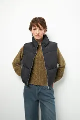 Chaleco puffer color beige, sin mangas, con cuello alto y cierre frontal con cremallera.