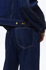 Jean de tiro alto confeccionado en denim de algodón lavado, con diseño de cinco bolsillos y piernas rectas de corte holgado. Cierre frontal con botón y cremallera.