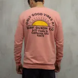 Buzo color salmón de algodón con cuello redondo, puños y cintura acanalados. Estampado en el frente con un sol y el texto "Only Good Vibes Surf Duxon Co. 3-77 Vissla St. California, USA 92672".