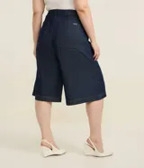 Bermuda tipo jorts de corte amplio y tiro medio, confeccionada en denim de algodón azul oscuro. Presenta diseño de cinco bolsillos, cierre frontal con botón y costuras en tono contrastante.