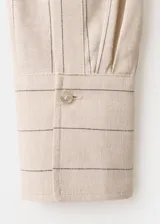 Vestido midi cruzado beige con sutiles rayas verticales oscuras, cuello camisero con solapa, mangas largas y cierre delantero cruzado.