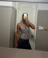 Top halter gris claro, ajustado al cuerpo, con escote pronunciado en V y cubierto de lentejuelas plateadas. El tejido es semitransparente.