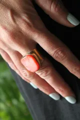 Anillo de diseño artesanal realizado en bronce con piedra central de color coral en formato rectangular. Cuenta con una estructura ajustable a presión.