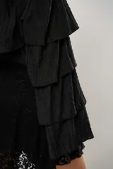 Blusa negra con un hombro descubierto y manga larga con volados.