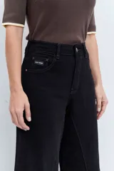 Jeans de tiro alto en color negro, con diseño de corte acampanado y paneles godet que aportan amplitud en el bajo. Presenta costuras visibles y cierre frontal con botón y cremallera.