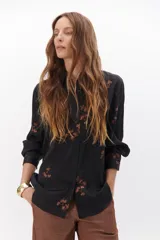 Camisa de manga larga color negro, confeccionada en poliéster sedoso, con bordados de lentejuelas en tonos cobrizos y botones a contratono.