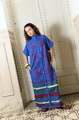Vestido largo de popelina de algodón azul, corte oversize, con cuello mao, mangas cortas, bolsillos laterales y cierre frontal de botones de arriba a abajo. Presenta estampado de flores rojas en gran tamaño y bandas horizontales multicolores en el ruedo.