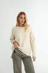 Sweater de punto en color beige, con cuello redondo y diseño de textura acanalada en la parte superior del pecho y hombros. Presenta mangas largas con puños ajustados y un corte holgado.