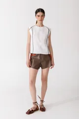 Blusa sin mangas color blanco, con cuello redondo y vivos de pespunte marrón en los hombros y costados.