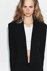 Blazer corto de corte recto con cuello de solapa, manga larga y hombreras. Presenta un diseño minimalista sin botones y forro interior a tono.