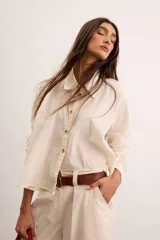 Camisa de algodón color crudo, con calce relajado, cuello clásico, botones delanteros, mangas largas con sutil volumen y ruedo asimétrico.
