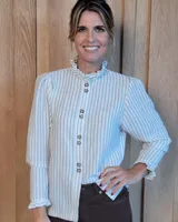 Camisa de manga larga con estampado de rayas verticales en tonos crudo y beige. Presenta cuello alto con volados, cierre frontal con botones dobles y puños con volados.