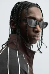 Cazadora de ajuste relajado, color marrón oscuro con bloques de color negro en las mangas. Presenta ribetes blancos que delinean los paneles y cuello alto con cierre frontal de cremallera. Los puños y el bajo son elásticos.