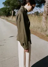 Chaqueta de lino color verde militar, diseño oversize con cuello alto, cierre oculto, manga larga con puño abotonado y cinturón ajustable en la cintura.