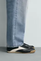 Zapatilla de cordones estilo retro, color negro con detalles en blanco y suela de goma color caramelo.