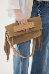 Cartera bandolera de gamuza azul marino con flecos en los laterales y solapa frontal decorada con detalle de cuero liso. Cuenta con asa ajustable y herrajes metálicos plateados.