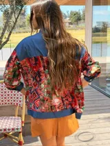Camisa oversize combinada que mezcla denim azul en la parte superior y mangas, con tela vintage de estampado geométrico y tribal multicolor en la espalda y mangas. Presenta cuello camisero y corte holgado.