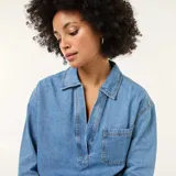 Camisa de jean de manga larga en tono azul medio, con cuello camisero, escote en V profundo y un bolsillo aplicado en el pecho.