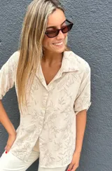 Camisa de seda color beige con estampado botánico en relieve bordado, de corte holgado, cuello camisero y cierre frontal con botones.