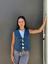 Chaleco de jean azul con cierre frontal mediante lazos ajustables, sin mangas y corte recto.