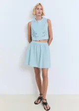 Falda corta evasé de algodón color celeste, con diseño fluido, detalles bordados y bajo festoneado. Cuenta con cierre de cremallera lateral.