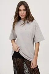 Remera oversized de manga corta y cuello redondo, de color negro con efecto acid wash y aplicación de strass en la parte superior.