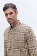 Camisa de manga larga confeccionada en viyela de algodón con estampado de cuadros en tonos beige y marrón. Presenta cuello clásico, cierre frontal con botones y un bolsillo aplicado en el pecho.