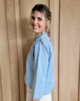 Blusa blanca de manga larga con cuello alto y volados en cuello y hombros.