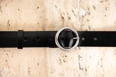 Cinto de cuero negro, ancho, con hebilla metálica plateada de forma ovalada o redonda.