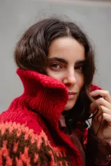 Saco tejido a mano con diseño jacquard en tonos rojo, naranja y marrón. Presenta cuello tipo polo, cierre frontal con botones grandes, mangas largas y tajos laterales en el ruedo.