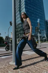 Chaleco jaspeado en tonos grises, con cuello redondo y sin mangas. Presenta cierre frontal con botones dorados y un cinturón fino negro con hebilla dorada.