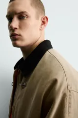 Cazadora de corte relajado confeccionada en algodón con efecto lavado. Presenta cuello de solapa en contraste de color negro, cierre frontal con cremallera oculta y alamares metálicos, bolsillos laterales de vivo y mangas largas.