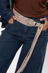 Faja de cuero gamuzado metalizado color visón, con curvatura anatómica, herraje metálico plateado y tiras largas con flecos para atar en nudo.