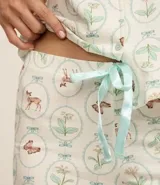 Conjunto de pijama de dos piezas, compuesto por una blusa de manga corta con cuello solapa, cierre frontal de botones y bolsillo en el pecho, y un short con cintura elástica y lazo de satén. El tejido es viscolycra con estampado de motivos florales y mariposas en círculos.