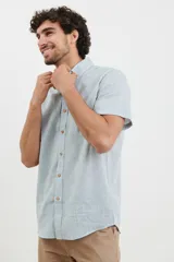 Camisa azul de manga corta, con cuello abotonado y bolsillo en el pecho.