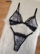 Conjunto de lencería compuesto por corpiño triangular y bombacha tipo tanga. El diseño combina microtul con estampado animal print y detalles de encaje negro en los bordes. El corpiño cuenta con cierre frontal y breteles regulables.