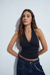 Top halter negro de silueta ajustada y diseño cropped, con escote profundo en V y frunce bajo el busto. Presenta espalda descubierta con lazo regulable en el cuello.