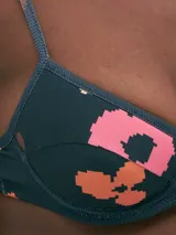 Corpiño de bikini con estampado abstracto en tonos rosa, naranja y marrón sobre fondo azul.